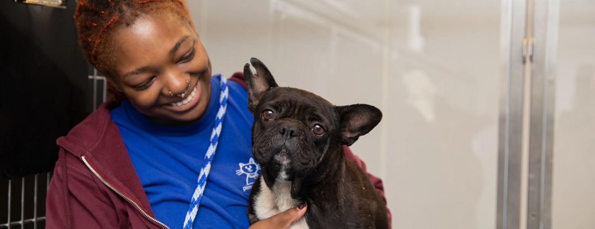 Shelter employee smiling at dog in her arms.